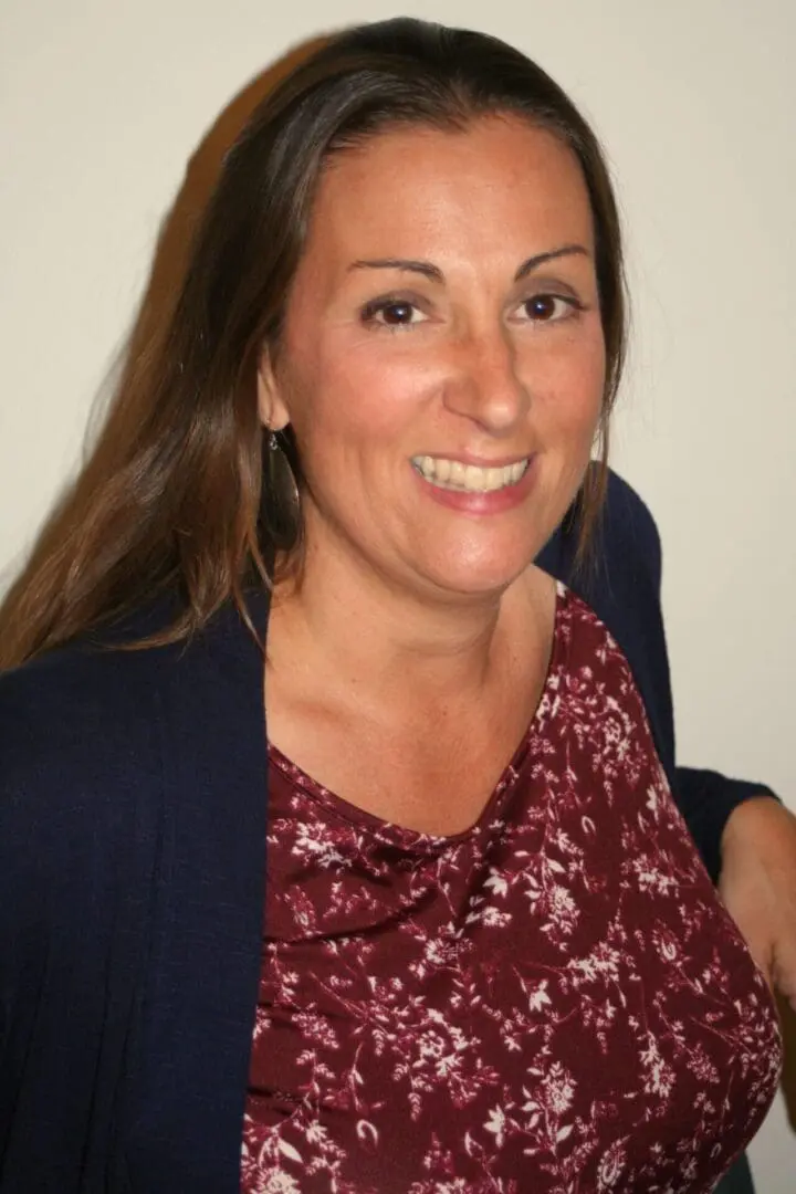 A woman in red shirt and jacket smiling.