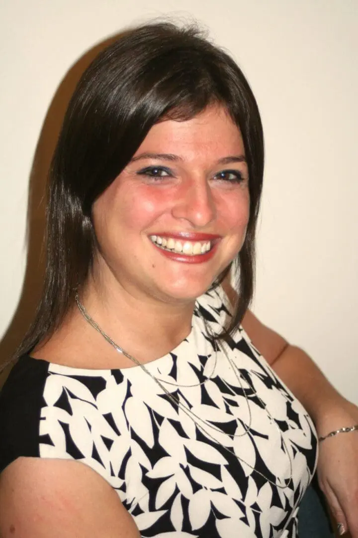 A woman smiling for the camera in front of a white wall.