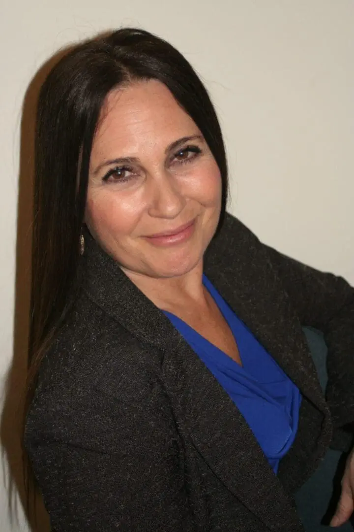A woman with long hair wearing a blue shirt and jacket.