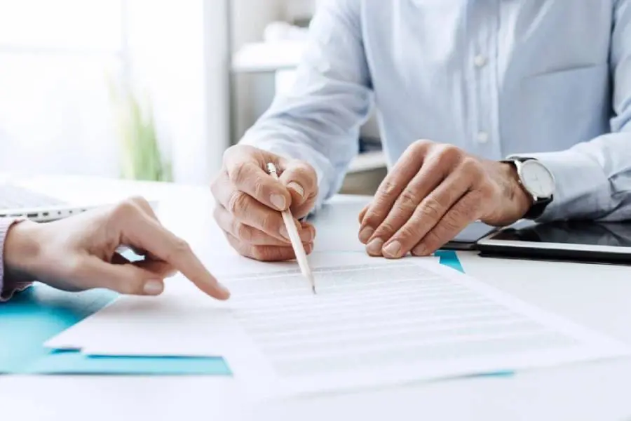 Two people are working on a paper with one hand and the other holding a pencil.