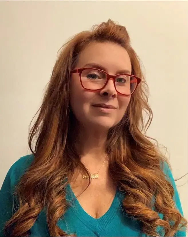 A woman with long red hair wearing glasses.