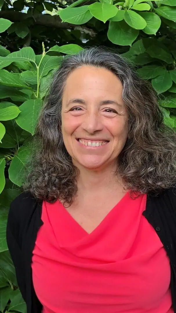 A woman with long hair and a red shirt is smiling.