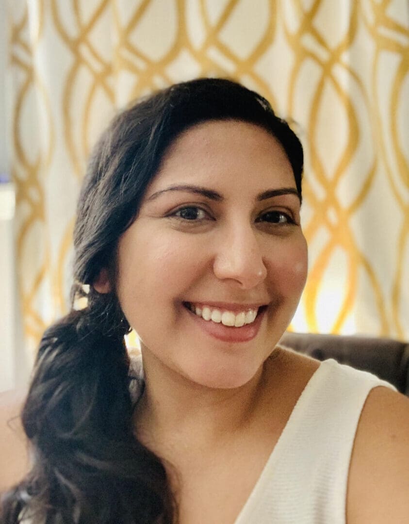 A woman smiling for the camera with her hair in a ponytail.