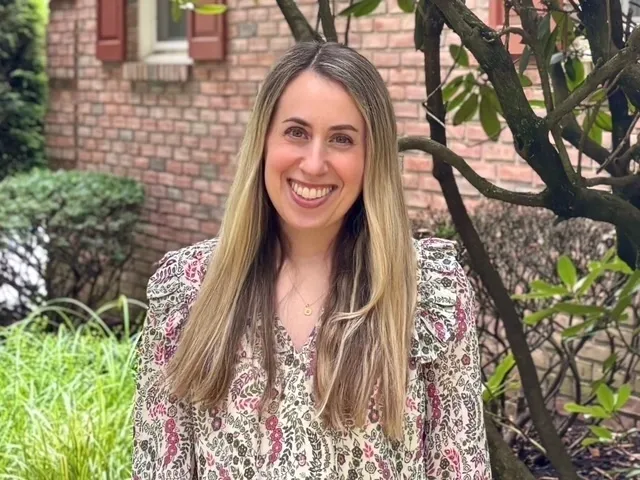 Smiling woman standing outside near brick wall.