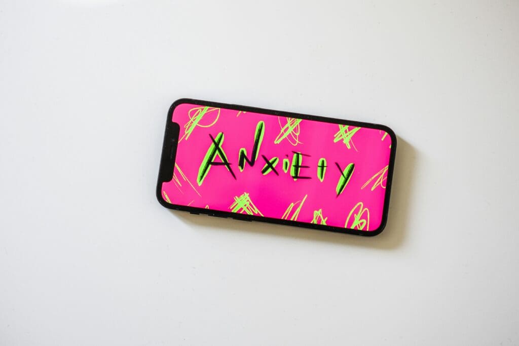 Smartphone displaying "Anxiety" on bright pink background.