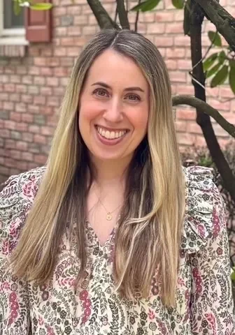 Smiling woman standing outside near brick wall.