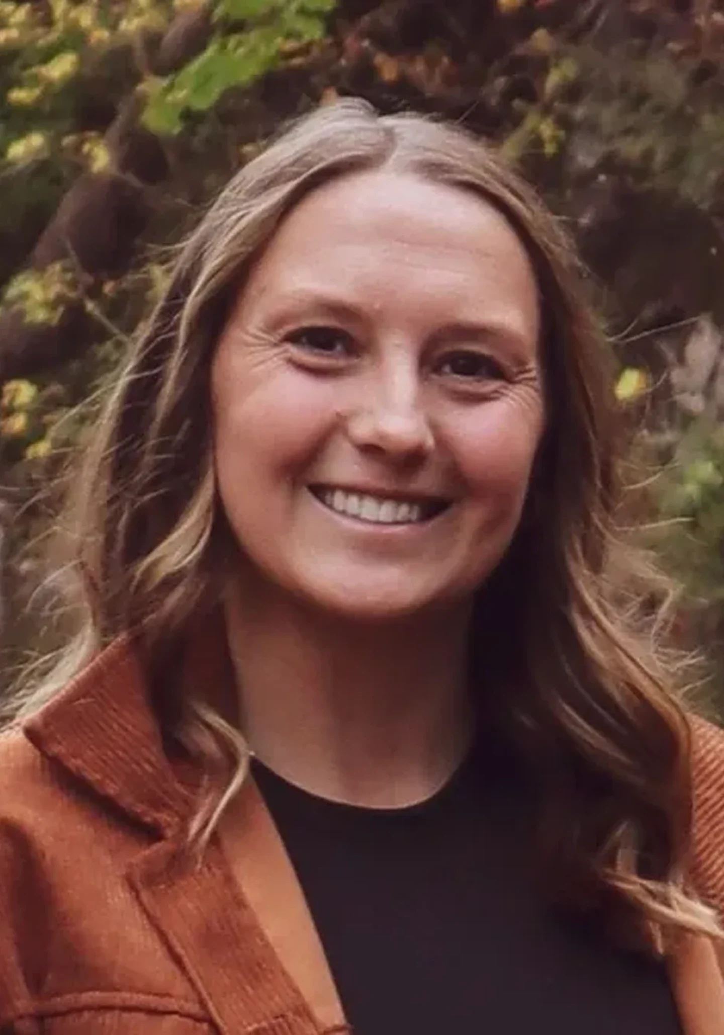 Smiling woman outdoors with autumn backdrop.